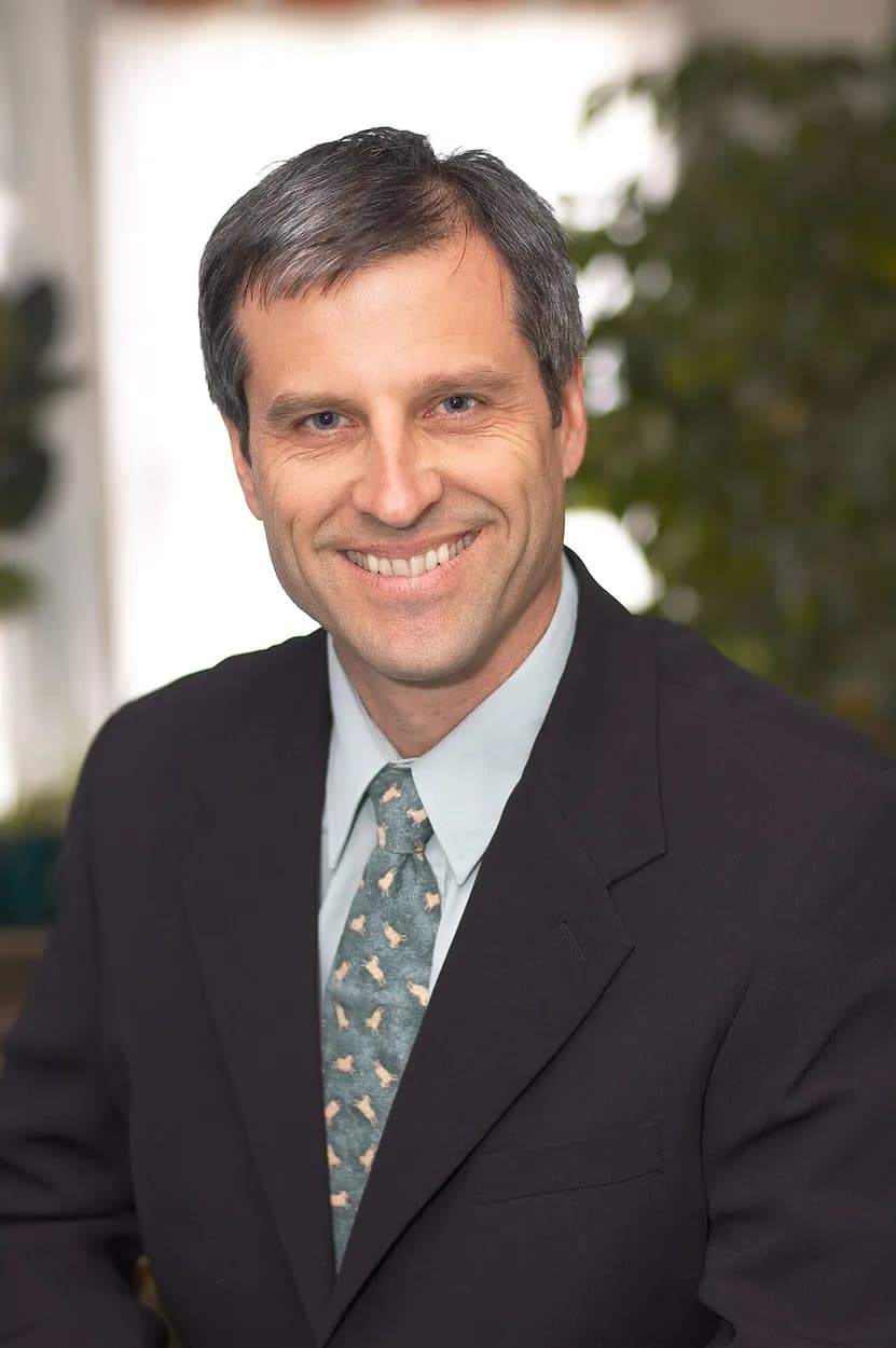 Portrait of Gene Baur smiling in a dark suit and green tie
