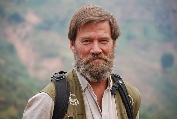 Portrait of Ian Redmond in a khaki field vest with a green hillside behind