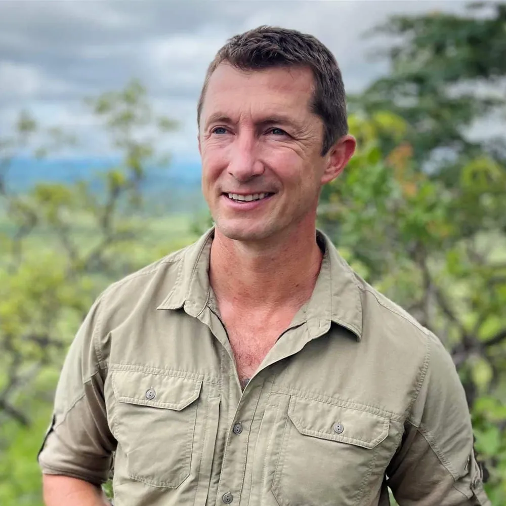 Portrait of Kurt Steiner smiling in a khaki field shirt in the bush