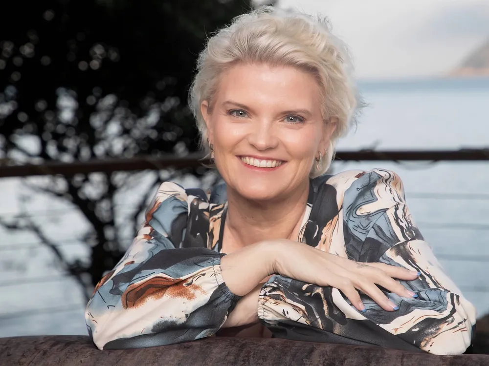 Portrait of Lisa Goosen smiling, with the ocean and a mountain behind
