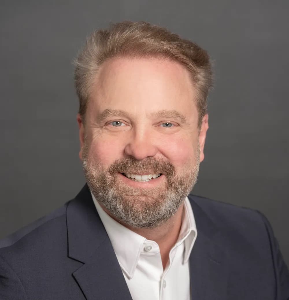 Portrait of Martin Lund smiling in a navy blazer against a grey backdrop