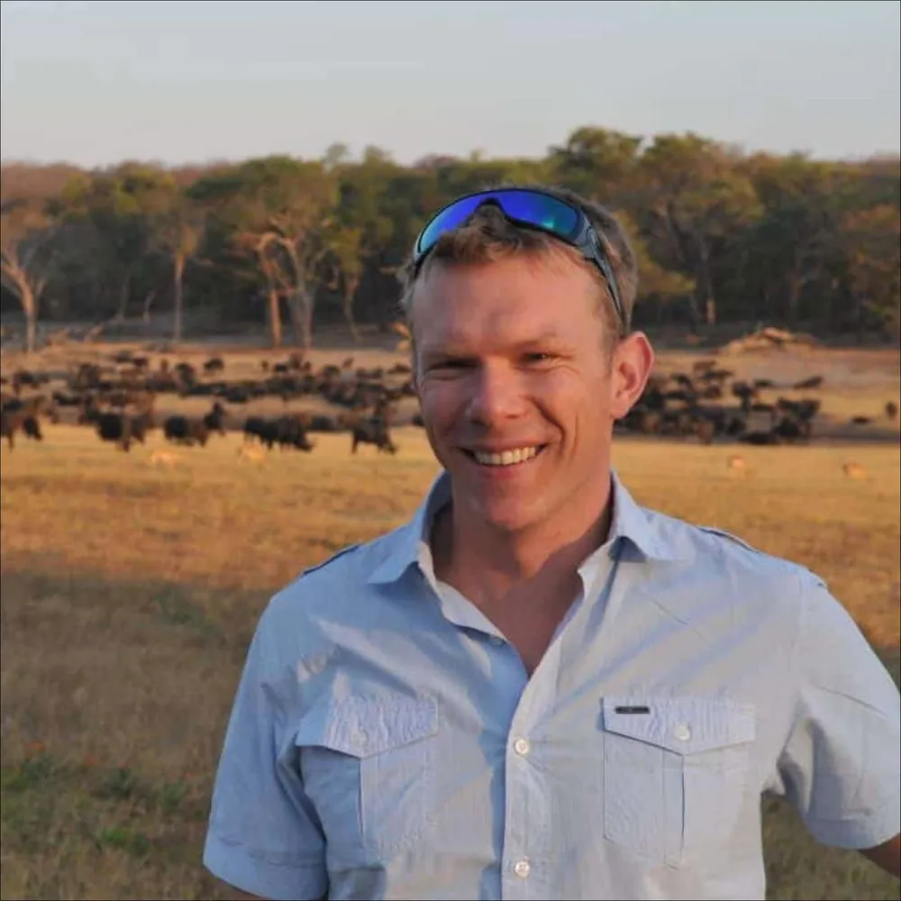 Portrait of Dr. Peter Lindsey smiling on the savanna with a buffalo herd behind