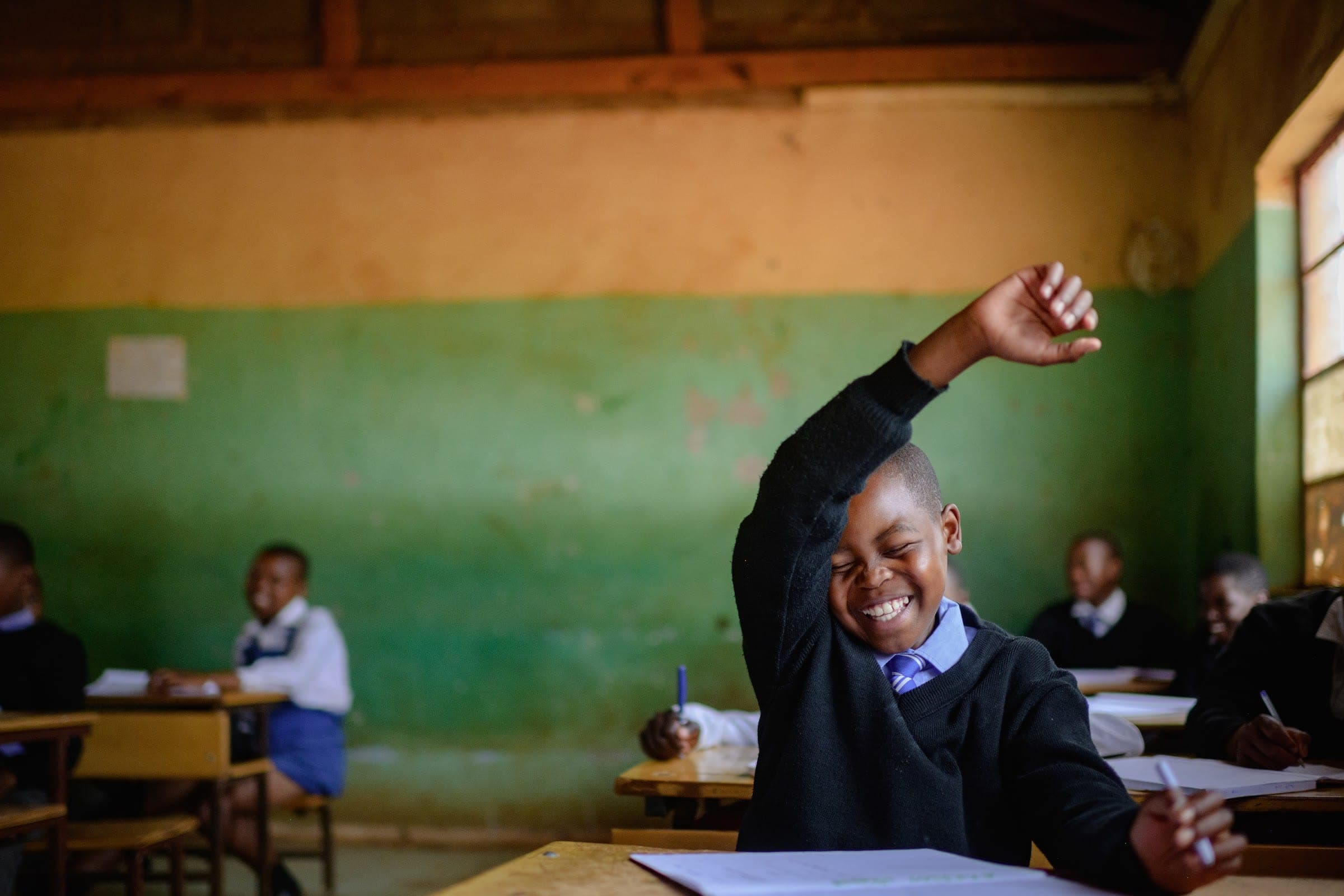 A smiling schoolboy raising his hand in a classroom