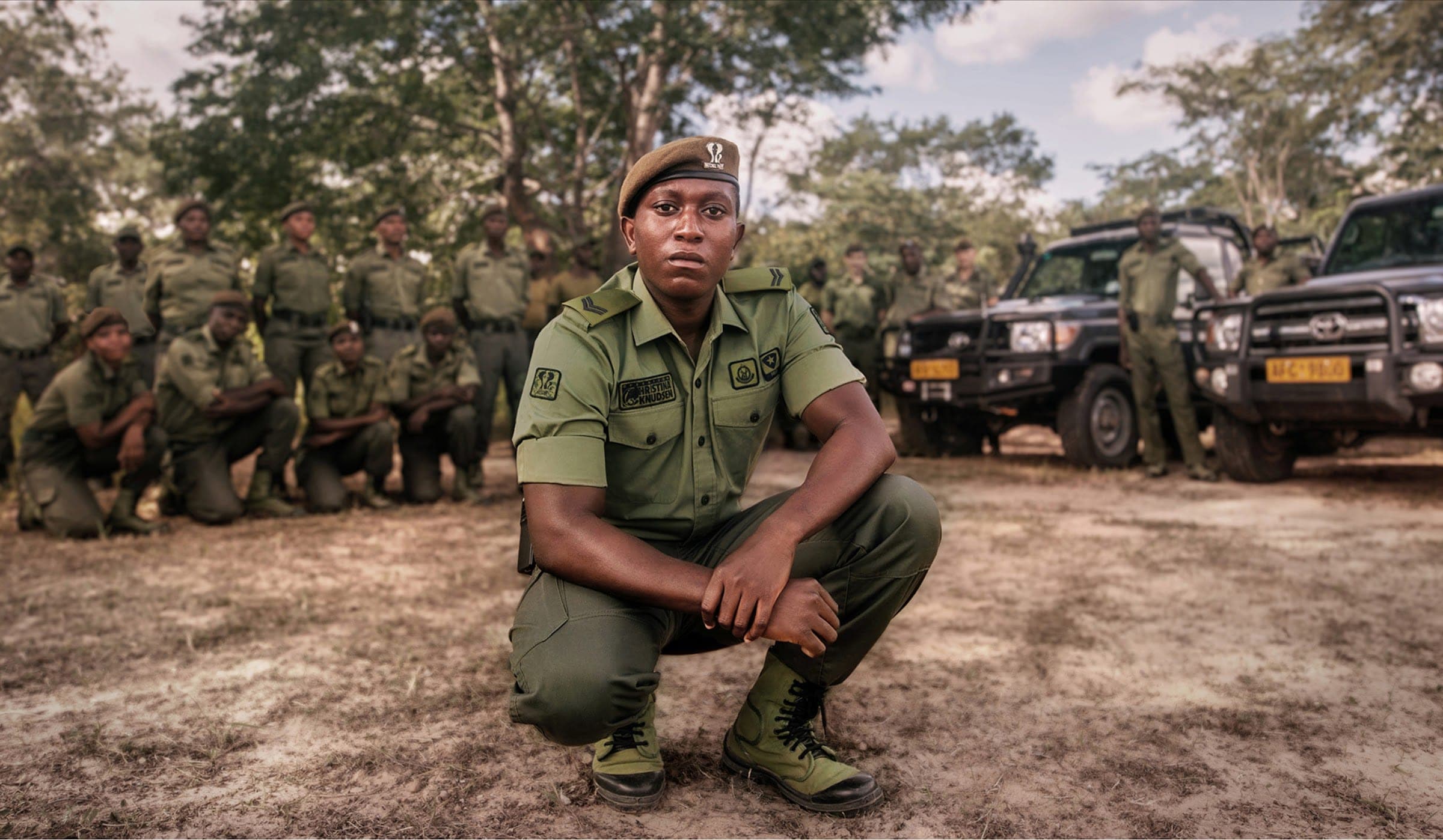 A ranger crouching in front of a ranger team and patrol vehicles in Chizarira