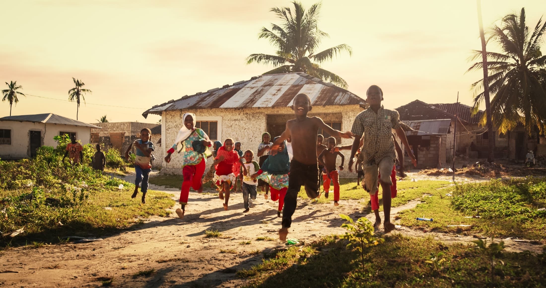 Children running and laughing along a village path at sunset