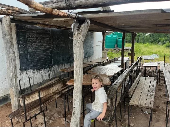 A child seated on a rough bench in an open-air classroom near Chizarira