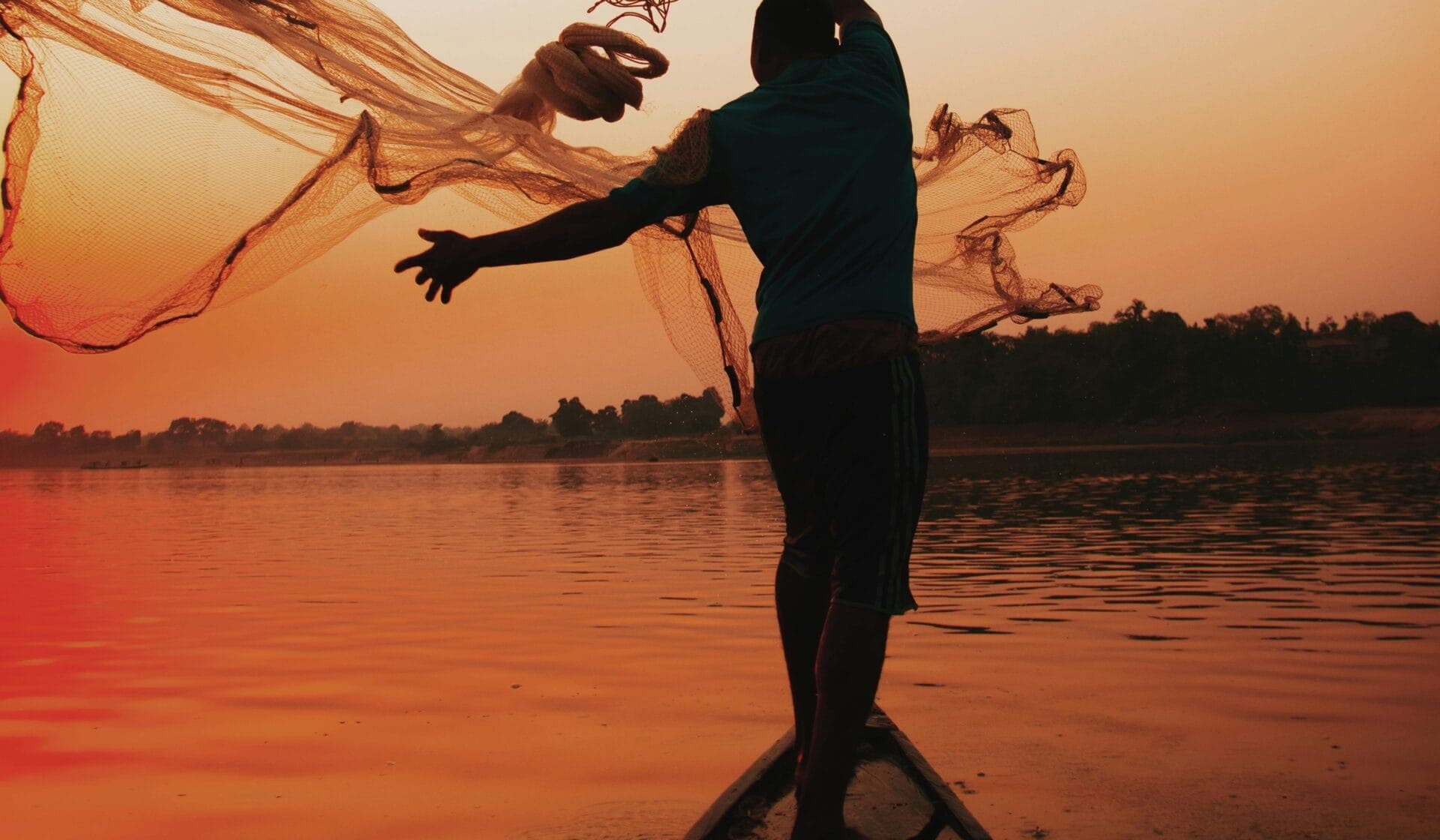 A fisherman casting a net into the shallows along Zanzibar's coastline at dusk